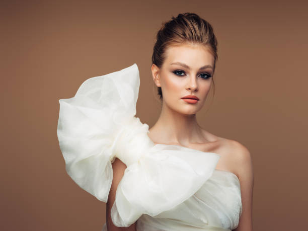 A bride with natural, elegant makeup, subtle eyeshadow, and a sophisticated updo poses in a white dress.